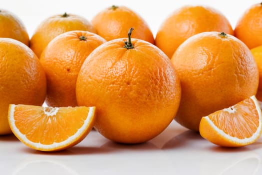 Close-up of fresh, vibrant oranges with some sliced wedges on a white background, emphasizing freshness, health, and natural citrus fruit.