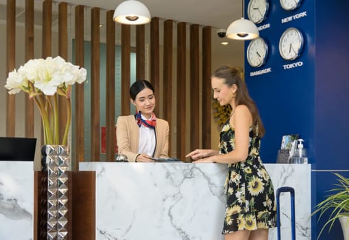 Friendly young receptionist helping and giving hotel check in information service to attractive female guest upon arrival