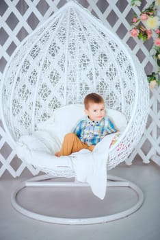The child is comfortably ensconced in a stylish decorative egg chair, radiating innocence and joy