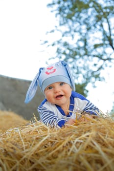 A kid in a charming hat with a rabbit happily playing on a haystack outdoors