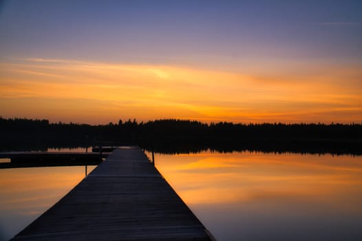 Wooden jetty at sunset on a Swedish lake. The colors of the sunset are reflected in the water. A bathing lake in the Scandinavian countryside