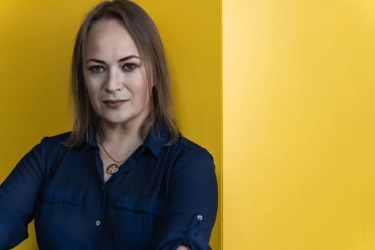 confident middle-aged woman in blue shirt against yellow backdrop.