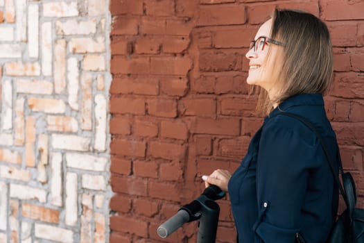 happy woman in glasses with electric scooter by brick wall.