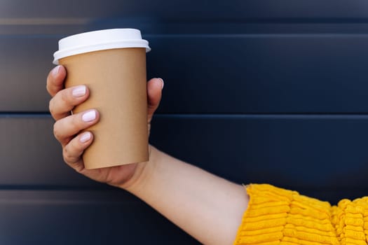 Hand holding disposable coffee cup on blue background.