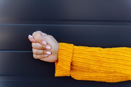 Woman hand making fig sign in yellow sleeve against dark striped background.