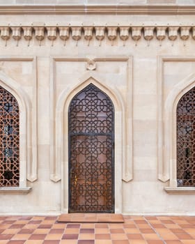 A beautifully crafted wooden door features an elaborate latticework design set against a traditional stone wall. The architectural details highlight the craftsmanship in this urban location.