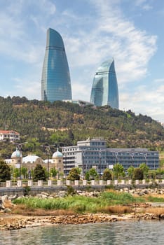 The iconic Flame Towers dominate the skyline of Baku, Azerbaijan, reflecting sunlight as they rise majestically above the landscape, surrounded by trees and a waterfront area