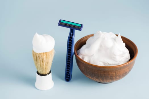 razor shaving brush bowl foam against blue backdrop. High resolution photo