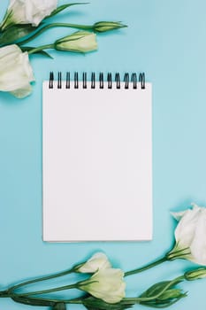 white eustoma flower with blank spiral notepad blue background. High resolution photo