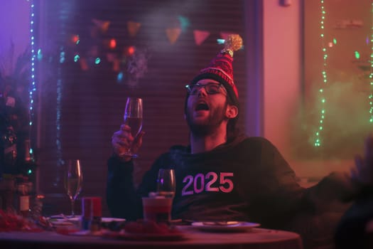 A person wearing a party hat raises a glass in celebration as colorful lights illuminate the space ushering in 2025.