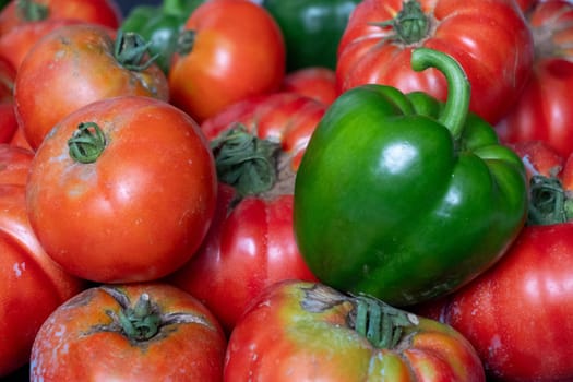 A bunch of red and green tomatoes are piled on top of each other. The green pepper is in the middle of the pile