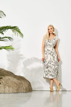 Elegant woman in floral pattern dress posing against white wall