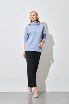 A modern fashion model poses in a relaxed stance, wearing a stylish blue sweater paired with classic black trousers, complemented by light blue heels
