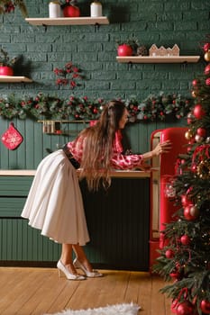 A woman opening a vintage red refrigerator amidst a beautifully decorated Christmas-themed kitchen. The kitchen is decorated with holiday ornaments, giving the space a warm and inviting atmosphere