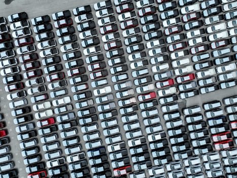 Aerial view of new cars stock at a large factory parking lot. Automotive industry, logistics operations, and vehicle storage for import and export. Key role in the global car market supply chain.