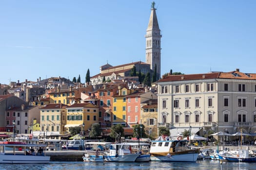 Rovinj, Croatia, Istria - September 29, 2023: Colorful tenement houses on the boulevard by South port over Adriatic Sea, moored boats and Saint Euphemia Church in a distance