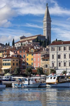 Rovinj, Croatia, Istria - September 29, 2023: Colorful tenement houses on the boulevard by South port over Adriatic Sea, moored boats and Saint Euphemia Church in a distance
