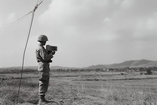 A soldier stands in a field holding a device, surrounded by open landscape and a cloudy sky.