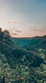A tranquil mountain valley with lush greenery and a beautiful sunrise. The early morning light casts soft pastel colors over the landscape, creating a serene and peaceful ambiance.