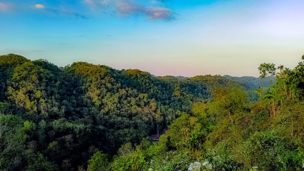 A tranquil mountain valley with lush greenery and a beautiful sunrise. The early morning light casts soft pastel colors over the landscape, creating a serene and peaceful ambiance.