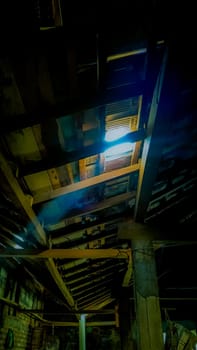 Atmospheric light beams penetrate an old wooden roof, creating a mysterious and rustic ambiance. The aged structure and shadows add a sense of history and intrigue to the scene.