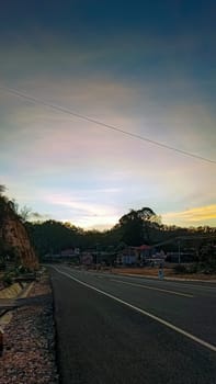 A serene landscape showcasing a quiet rural road with a stunning sunset in the background. The peaceful countryside setting evokes tranquility and the beauty of nature.