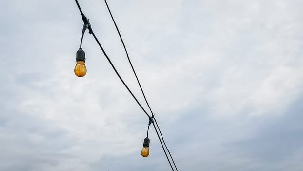 A string of lights hanging from a power line. The lights are yellow and are hanging from the wires