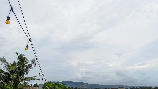 A string of lights hanging from a power line. The lights are yellow and are hanging from the wires