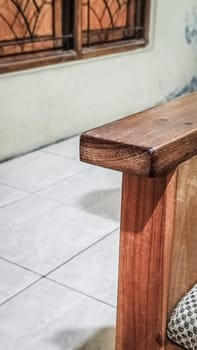 A detailed view of a wooden chair armrest, highlighting its texture and design. The cozy indoor setting includes tiled flooring and a window.