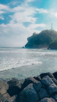 A rocky shoreline with a large rock formation in the background. The water is calm and the sky is blue