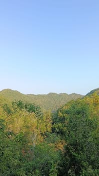 A serene mountain landscape bathed in sunlight, showcasing lush green forests beneath a clear blue sky. Perfect for nature lovers seeking peace in a tranquil environment.