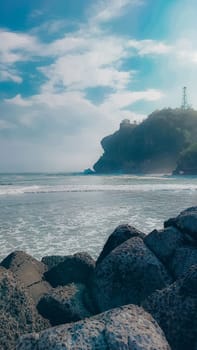 A rocky shoreline with a large rock formation in the background. The water is calm and the sky is blue