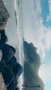 A rocky shoreline with a large rock formation in the background. The water is calm and the sky is blue