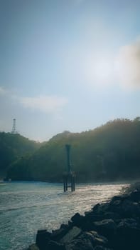 A rocky shoreline with a large rock formation in the background. The water is calm and the sky is blue