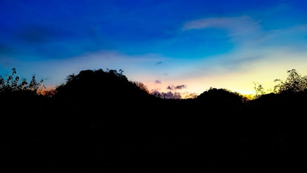 A picturesque silhouette of a landscape set against a vibrant sunset sky, showcasing a blend of blue, orange, and yellow hues. Perfect for themes of nature, tranquility, and beauty.