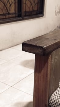 A detailed view of a wooden chair armrest, highlighting its texture and design. The cozy indoor setting includes tiled flooring and a window.