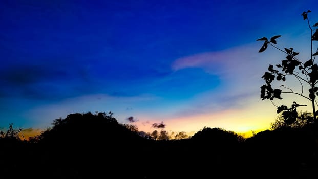 A picturesque silhouette of a landscape set against a vibrant sunset sky, showcasing a blend of blue, orange, and yellow hues. Perfect for themes of nature, tranquility, and beauty.