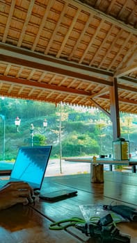 A serene outdoor workspace with a laptop on a wooden table, offering a peaceful view of nature and distant people enjoying the scenery.