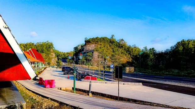 A peaceful roadside view featuring a red-roofed building, clear blue sky, and greenery along a mountain road, creating a tranquil atmosphere.