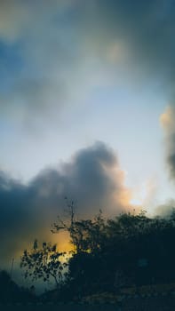 Captivating sunset scene with a silhouette of trees against dramatic, colorful clouds. The warm tones evoke feelings of tranquility and peace, offering a perfect example of nature's breathtaking beauty.