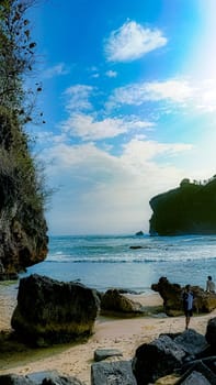 A rocky shoreline with a large rock formation in the background. The water is calm and the sky is blue