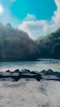 A rocky shoreline with a large rock formation in the background. The water is calm and the sky is blue