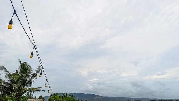 A string of lights hanging from a power line. The lights are yellow and are hanging from the wires