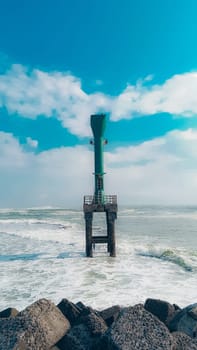 A solitary beacon tower stands on rocky coast, surrounded by the ocean under a clear blue sky. Perfect for themes of solitude, navigation, and coastal landscapes.