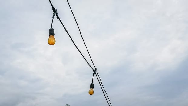 A string of lights hanging from a power line. The lights are yellow and are hanging from the wires
