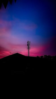 A silhouette of a communication tower stands prominently against a stunning pink and blue sky at sunset, evoking a sense of tranquility and modern technology.