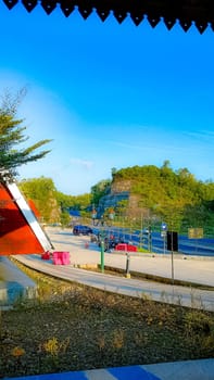 A peaceful roadside view featuring a red-roofed building, clear blue sky, and greenery along a mountain road, creating a tranquil atmosphere.