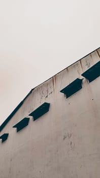 A minimalist view of a weathered industrial warehouse exterior with simple, clean lines and architectural details that evoke a vintage, rustic charm under a soft, overcast sky.