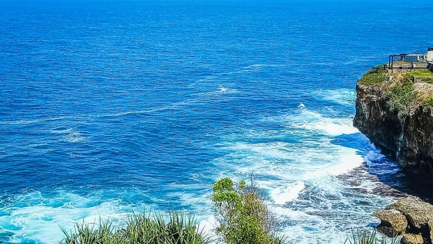Stunning view of a rocky cliff overlooking the vast, blue ocean with waves crashing below. The harmonious blend of sea and sky offers a sense of peace and tranquility.