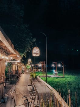 A charming outdoor cafe lit by warm lanterns against a tranquil nighttime backdrop, offering a serene and romantic atmosphere amidst green surroundings.